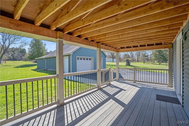 wooden terrace featuring a detached garage, an outdoor structure, and a lawn