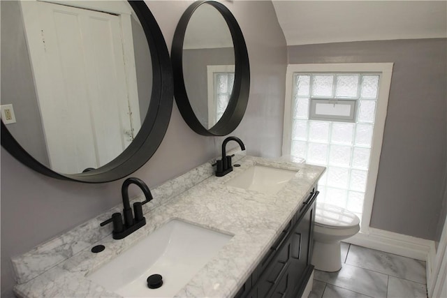 full bath with toilet, double vanity, a sink, and vaulted ceiling