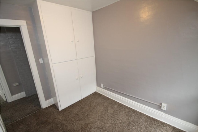 unfurnished bedroom featuring baseboards, a closet, and dark colored carpet