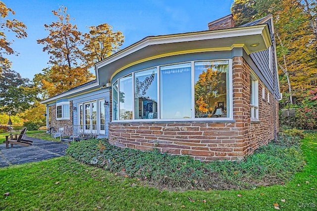 view of side of property featuring brick siding, french doors, a chimney, and a lawn