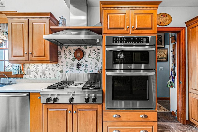kitchen with brown cabinetry, exhaust hood, light countertops, wallpapered walls, and appliances with stainless steel finishes