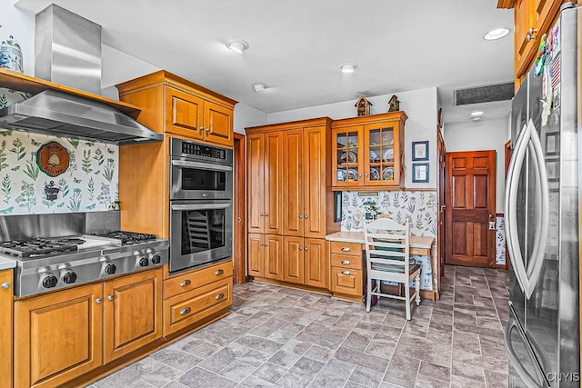 kitchen with brown cabinetry, stainless steel appliances, island range hood, backsplash, and glass insert cabinets