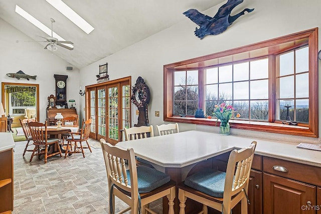 dining space featuring a ceiling fan, a skylight, stone finish flooring, and high vaulted ceiling