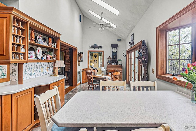 dining space with ceiling fan, a skylight, and high vaulted ceiling