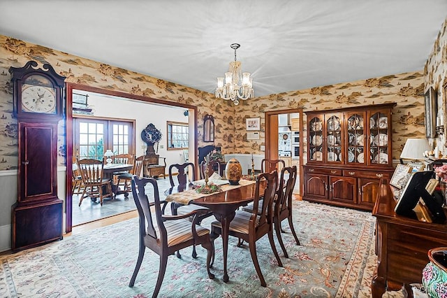 dining area featuring a wainscoted wall, a notable chandelier, light wood-type flooring, and wallpapered walls