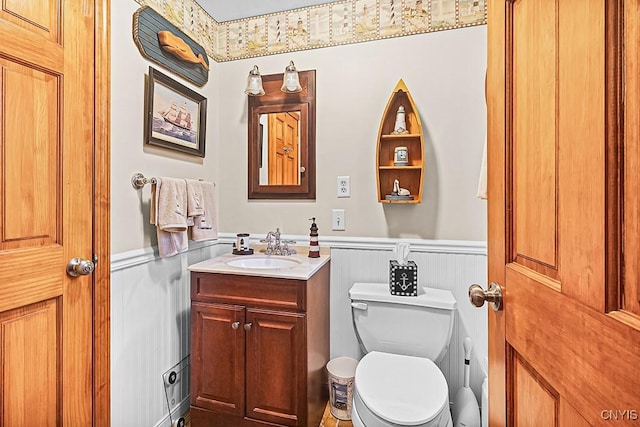 bathroom with vanity, toilet, a decorative wall, and a wainscoted wall