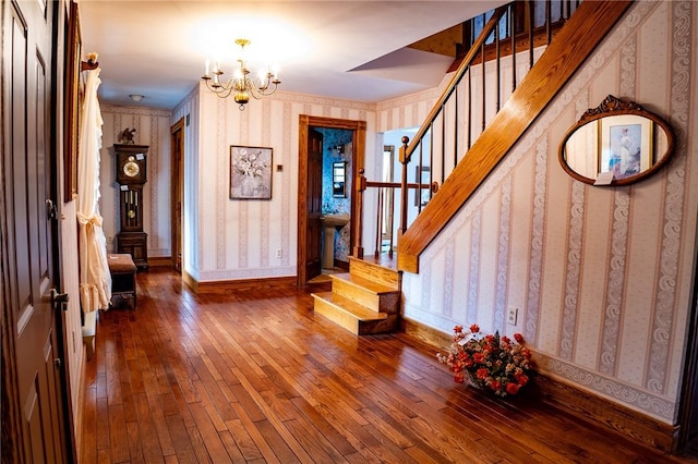 foyer entrance with stairs, hardwood / wood-style floors, an inviting chandelier, and wallpapered walls