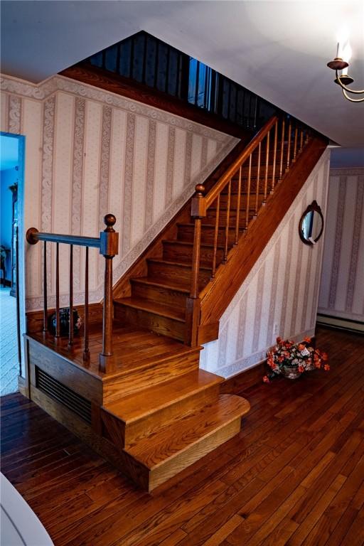 stairs with a chandelier, wallpapered walls, visible vents, and hardwood / wood-style floors