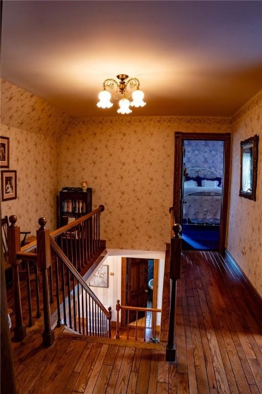 stairway with wallpapered walls, a chandelier, and wood-type flooring