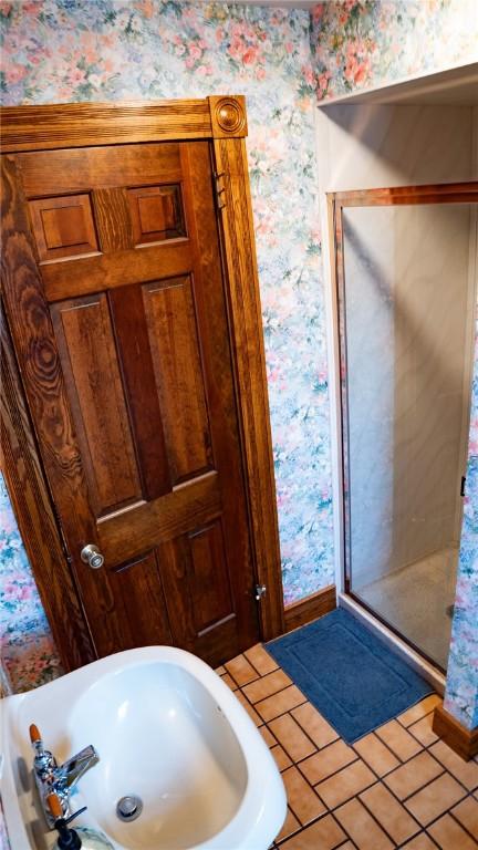 full bath featuring wallpapered walls, tile patterned flooring, a stall shower, and a sink