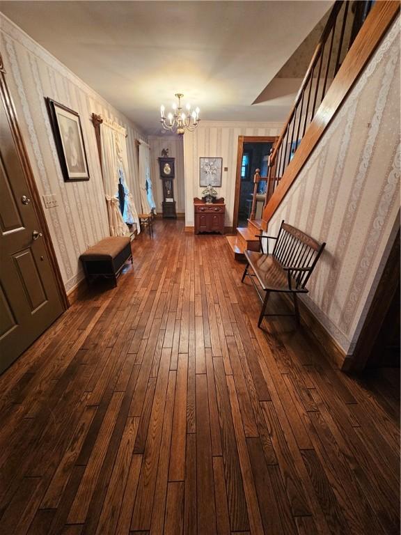 entrance foyer featuring wallpapered walls, baseboards, a chandelier, stairway, and dark wood-style floors