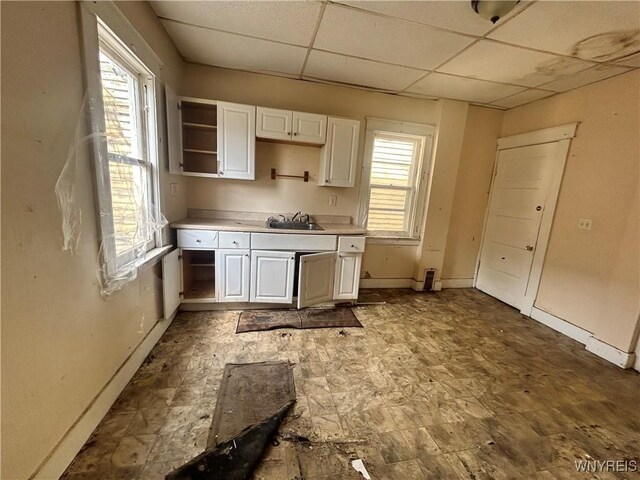 kitchen with baseboards, a sink, a paneled ceiling, light countertops, and white cabinets
