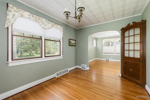 spare room with arched walkways, ornamental molding, visible vents, and wood finished floors