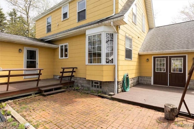 rear view of house with roof with shingles, a deck, a patio, and french doors