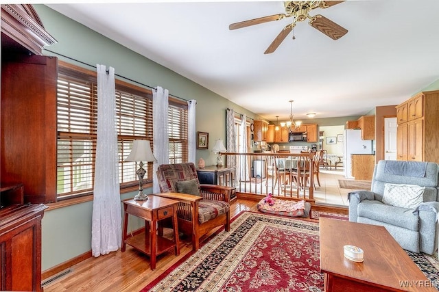 living room with plenty of natural light, baseboards, ceiling fan with notable chandelier, and light wood-style floors