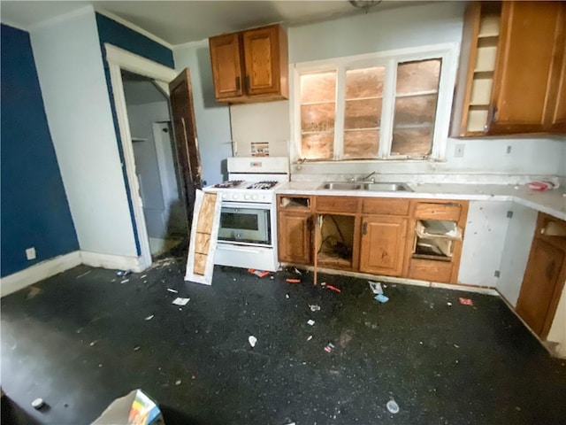 kitchen with brown cabinets, baseboards, a sink, and white range with gas cooktop