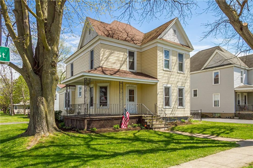 victorian house with a front lawn, roof with shingles, and covered porch