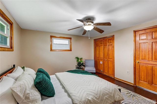 bedroom with dark wood-style flooring, ceiling fan, a closet, and baseboards