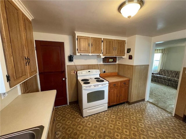 kitchen with a sink, dark floors, a wainscoted wall, brown cabinets, and white range with electric cooktop