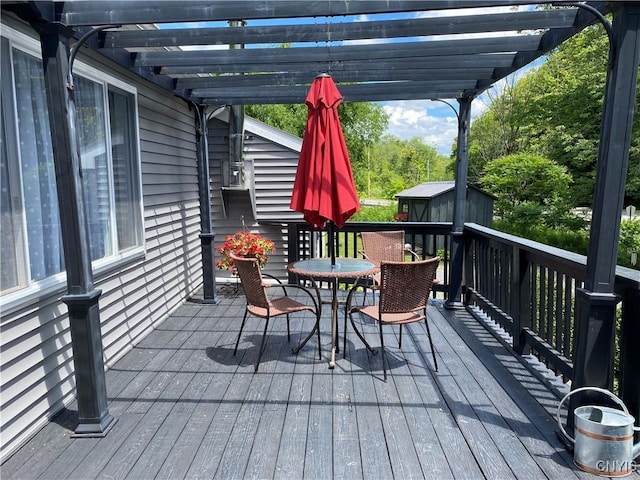 wooden deck with an outbuilding, outdoor dining space, a pergola, and a storage unit