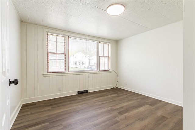 empty room featuring baseboards, visible vents, and dark wood-type flooring