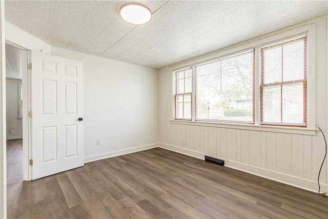empty room featuring visible vents, dark wood-style flooring, and baseboards