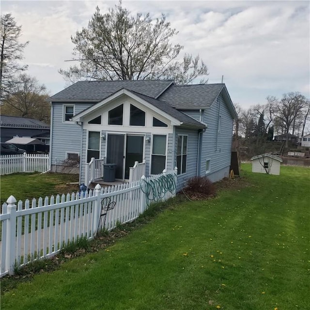 rear view of house with fence private yard, roof with shingles, an outbuilding, and a lawn