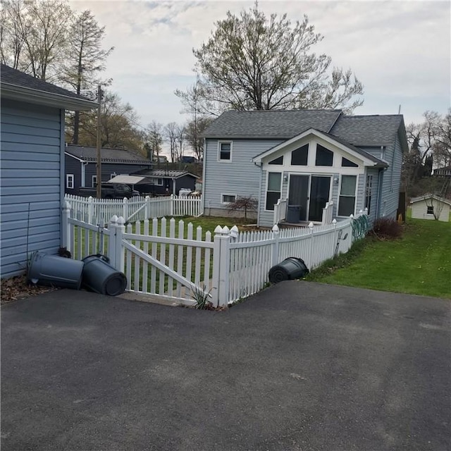 back of property featuring a yard, a shingled roof, and a fenced front yard
