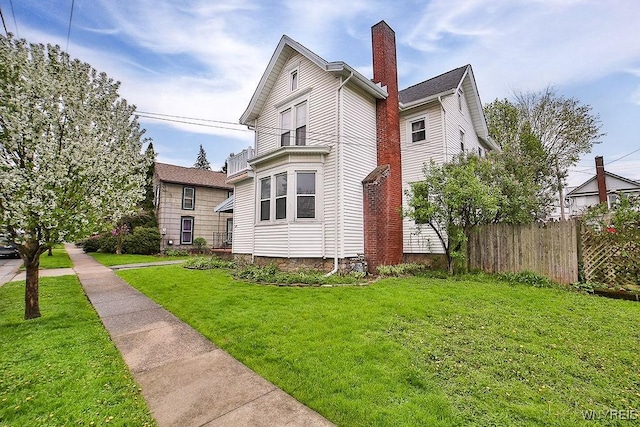 view of side of home featuring a chimney, fence, and a lawn
