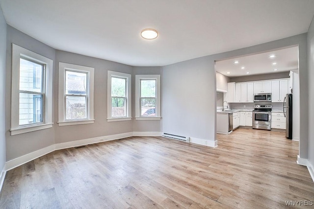 unfurnished living room featuring a sink, light wood-type flooring, visible vents, baseboards, and a baseboard heating unit