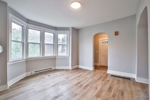 unfurnished room featuring a healthy amount of sunlight, visible vents, a baseboard radiator, and arched walkways