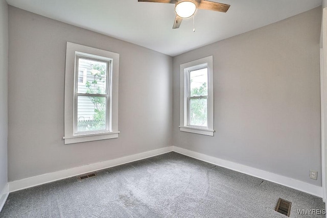 unfurnished room with a wealth of natural light, dark colored carpet, and visible vents