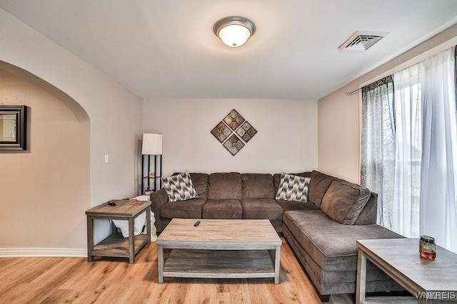 living area with visible vents, light wood-style flooring, baseboards, and arched walkways