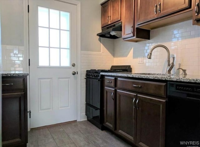 kitchen with under cabinet range hood, light stone countertops, black appliances, and a sink