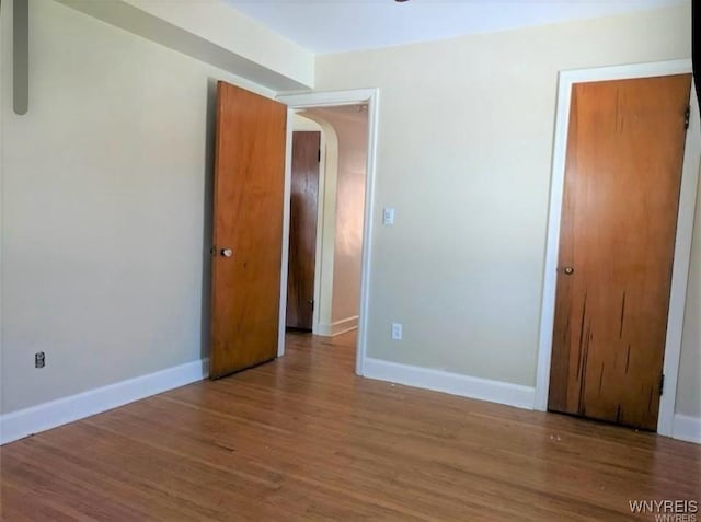 unfurnished bedroom with baseboards, arched walkways, a closet, and wood finished floors