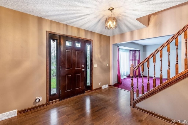 foyer featuring a chandelier, wood finished floors, baseboards, stairway, and a textured ceiling