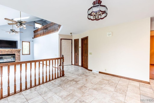 unfurnished room featuring a ceiling fan, baseboards, and a brick fireplace
