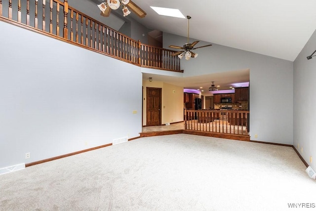 unfurnished living room with ceiling fan, carpet flooring, a skylight, baseboards, and high vaulted ceiling