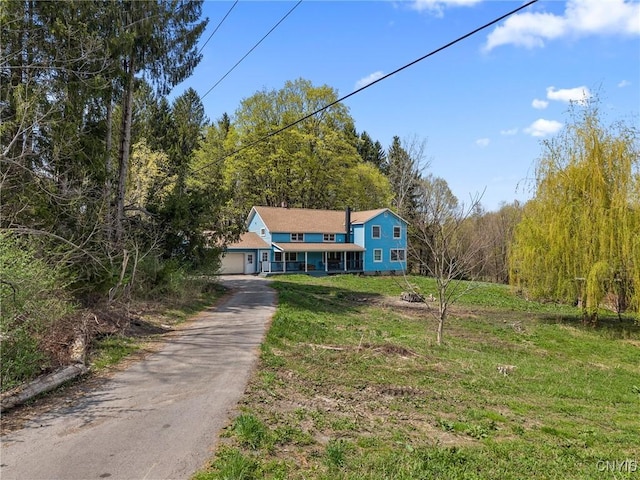 view of front facade featuring a wooded view, aphalt driveway, and a front lawn