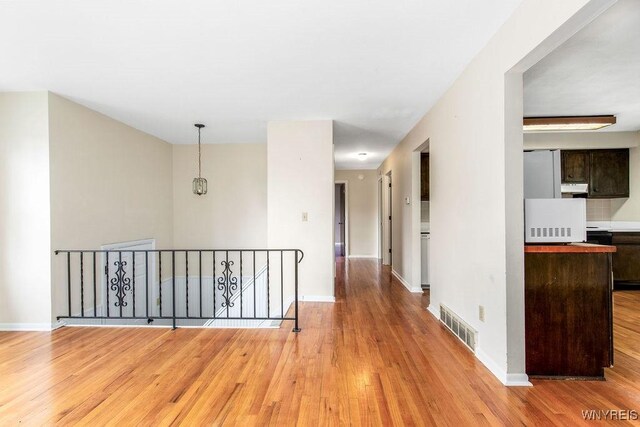 corridor featuring baseboards, light wood-style floors, an upstairs landing, and visible vents