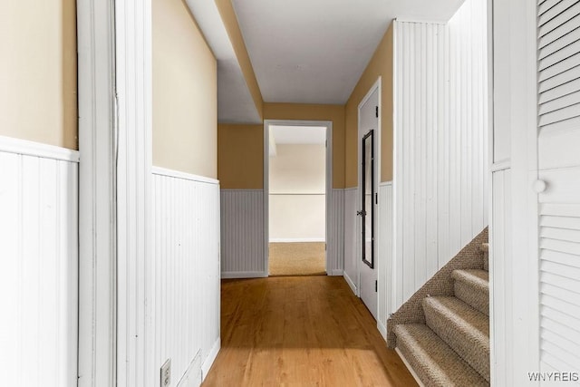 hallway with stairway, light wood finished floors, and wainscoting