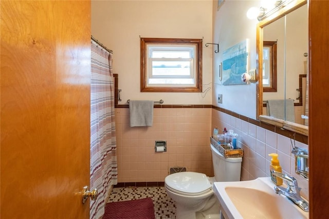 full bath with tile walls, toilet, a sink, curtained shower, and a wainscoted wall