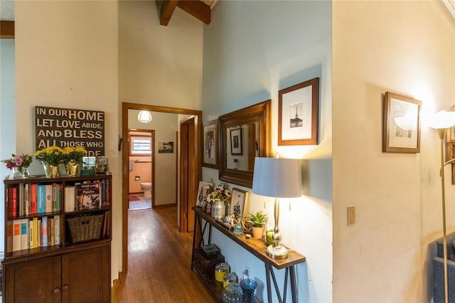 hall with beam ceiling, a high ceiling, and wood finished floors