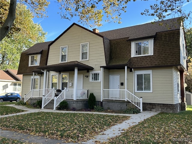 colonial inspired home with roof with shingles, a gambrel roof, a front lawn, and a chimney