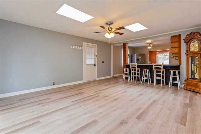 living room with light wood finished floors, baseboards, a skylight, and ceiling fan