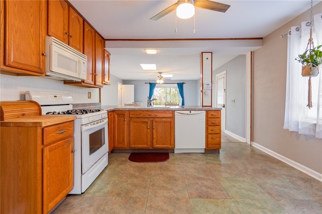 kitchen featuring a ceiling fan, white appliances, a peninsula, brown cabinets, and a skylight