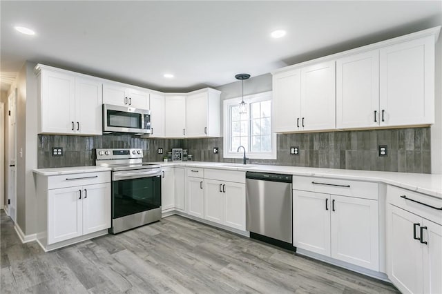 kitchen with a sink, recessed lighting, light countertops, white cabinets, and appliances with stainless steel finishes
