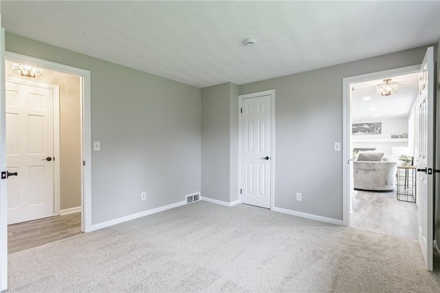 unfurnished bedroom featuring an inviting chandelier, visible vents, baseboards, and carpet floors