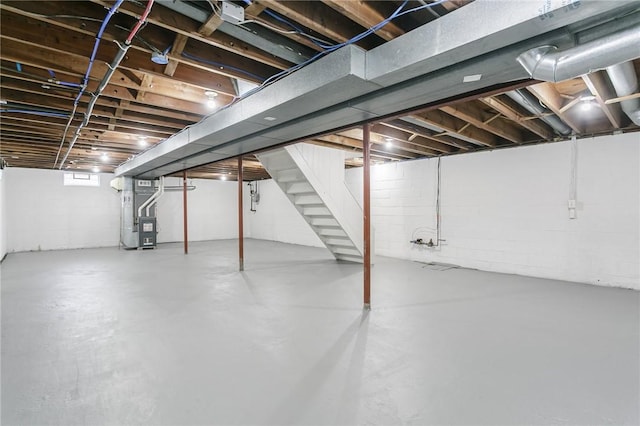 basement with heating unit, concrete block wall, and stairs