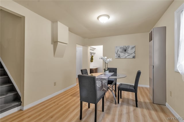 dining space with light wood-type flooring, baseboards, and stairs